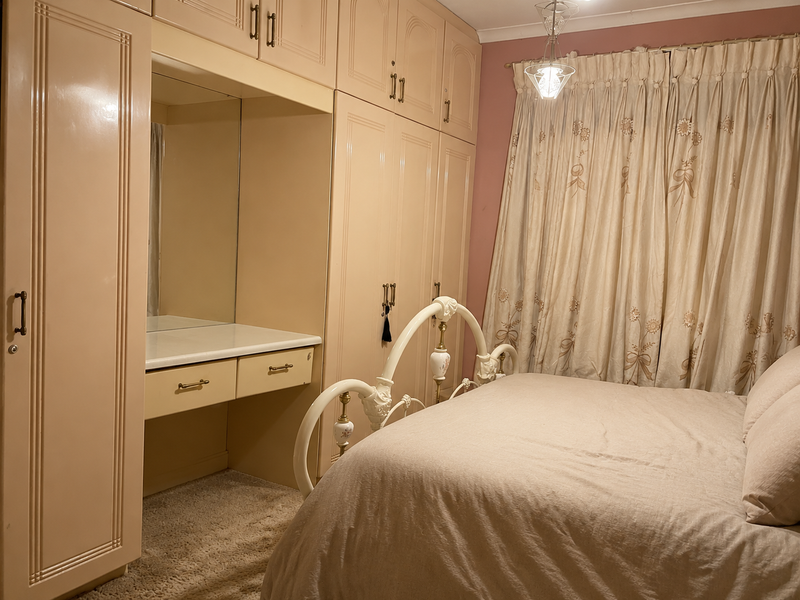 A bedroom featuring extensive built-in cabinetry with an integrated vanity and mirror, complemented by carpeted flooring and a central pendant light fixture.