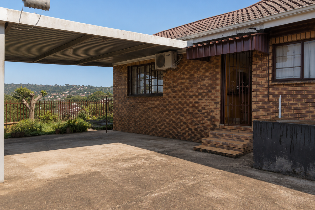 Rear exterior view featuring a brick facade, covered carport area, security gate, and concrete driveway with views of the surrounding landscape.