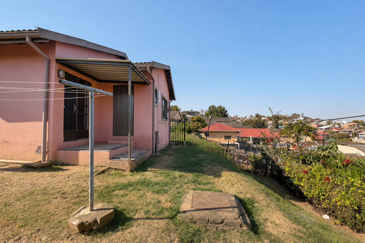 Rear view of the property featuring a covered patio area, metal roofing, and a sloped garden with surrounding neighbourhood views.