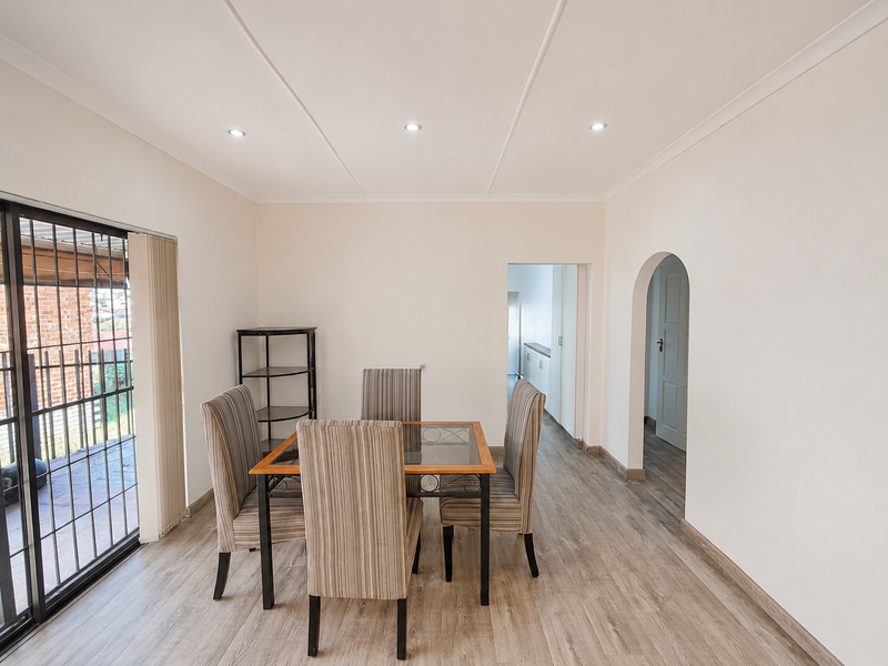 A bright dining area featuring modern laminate flooring, recessed downlights, and a sliding glass door leading to the exterior.
