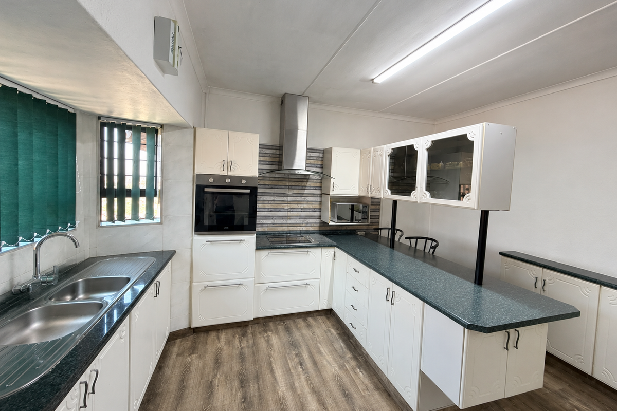 A functional kitchen featuring white cabinetry, dark countertops, a built-in oven, extractor fan, and a breakfast bar area with laminate flooring.