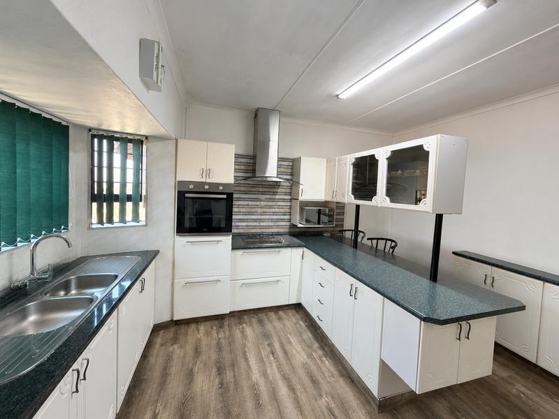 A functional kitchen featuring white cabinetry, dark countertops, a built-in oven, extractor fan, and a breakfast bar area with laminate flooring.