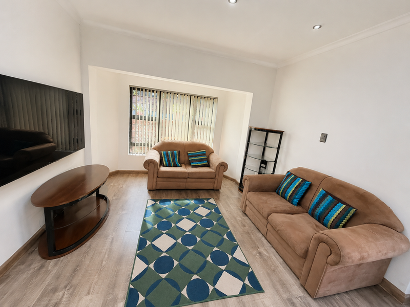 A bright living room featuring laminate flooring, recessed downlights, and a large window with vertical blinds.