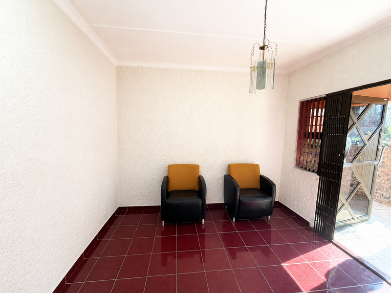 A bright living area featuring red tiled flooring, textured walls, and a decorative hanging light fixture, with direct access to an outdoor patio.