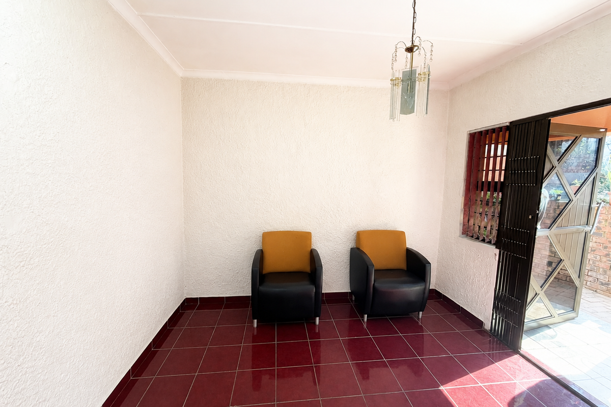 A bright living area featuring red tiled flooring, textured walls, and a decorative hanging light fixture, with direct access to an outdoor patio.