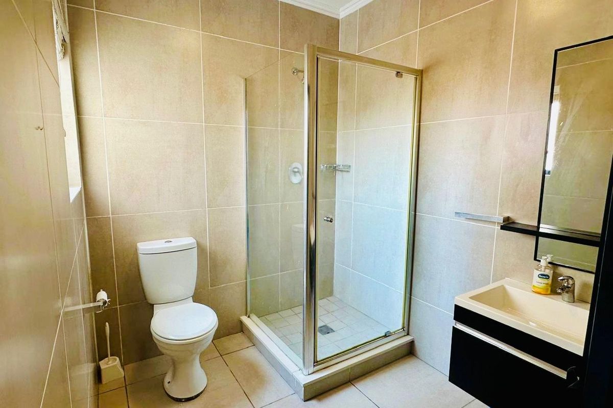 A clean, modern bathroom featuring a glass-enclosed shower, a wall-mounted vanity with a mirror, and neutral floor-to-ceiling wall tiles.