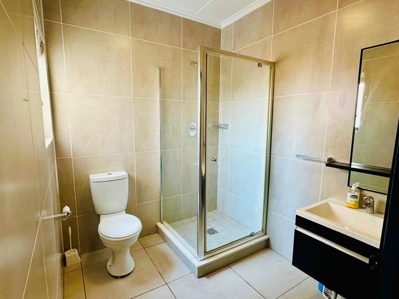A clean, modern bathroom featuring a glass-enclosed shower, a wall-mounted vanity with a mirror, and neutral floor-to-ceiling wall tiles.