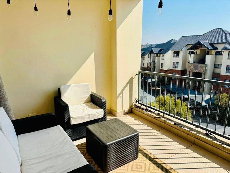 A covered balcony featuring tiled flooring, a metal safety balustrade, and pendant lighting, offering an elevated view of the surrounding apartment complex.