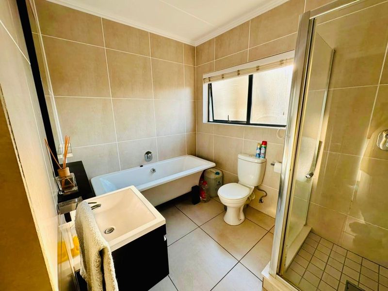 A functional bathroom featuring a bathtub, separate shower enclosure, toilet, and a modern vanity basin with neutral wall and floor tiling.