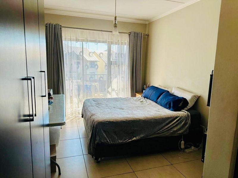 A well-lit bedroom featuring tiled flooring, built-in cupboards, and a sliding glass door providing access to an outdoor balcony area.