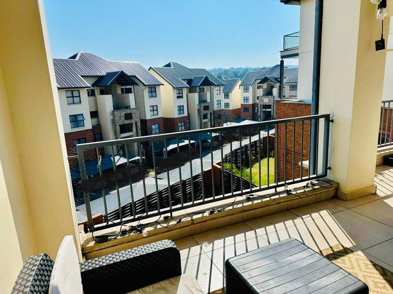 A covered balcony featuring tiled flooring and a metal balustrade, offering an elevated view of the surrounding apartment complex.