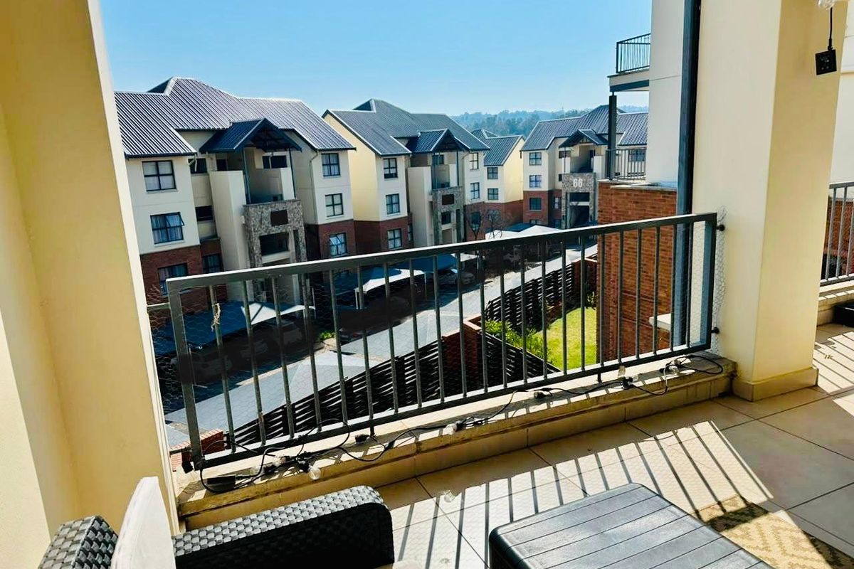 A covered balcony featuring tiled flooring and a metal balustrade, offering an elevated view of the surrounding apartment complex.