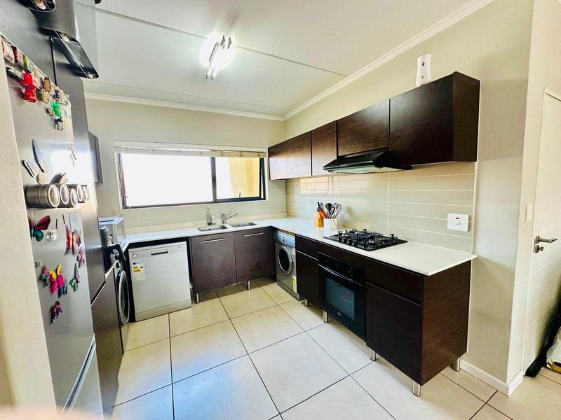 A functional kitchen featuring dark wood cabinetry, white stone countertops, a built-in gas hob, oven, extractor fan, and tiled flooring.