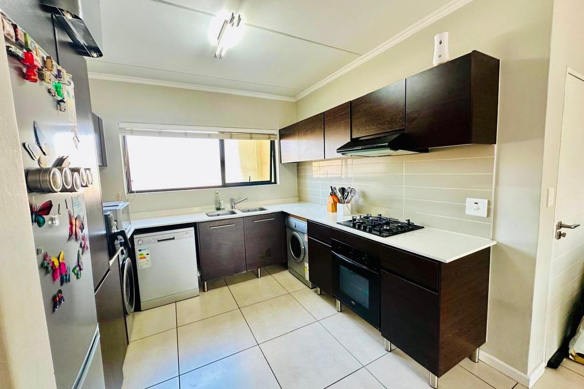 A functional kitchen featuring dark wood cabinetry, white stone countertops, a built-in gas hob, oven, extractor fan, and tiled flooring.