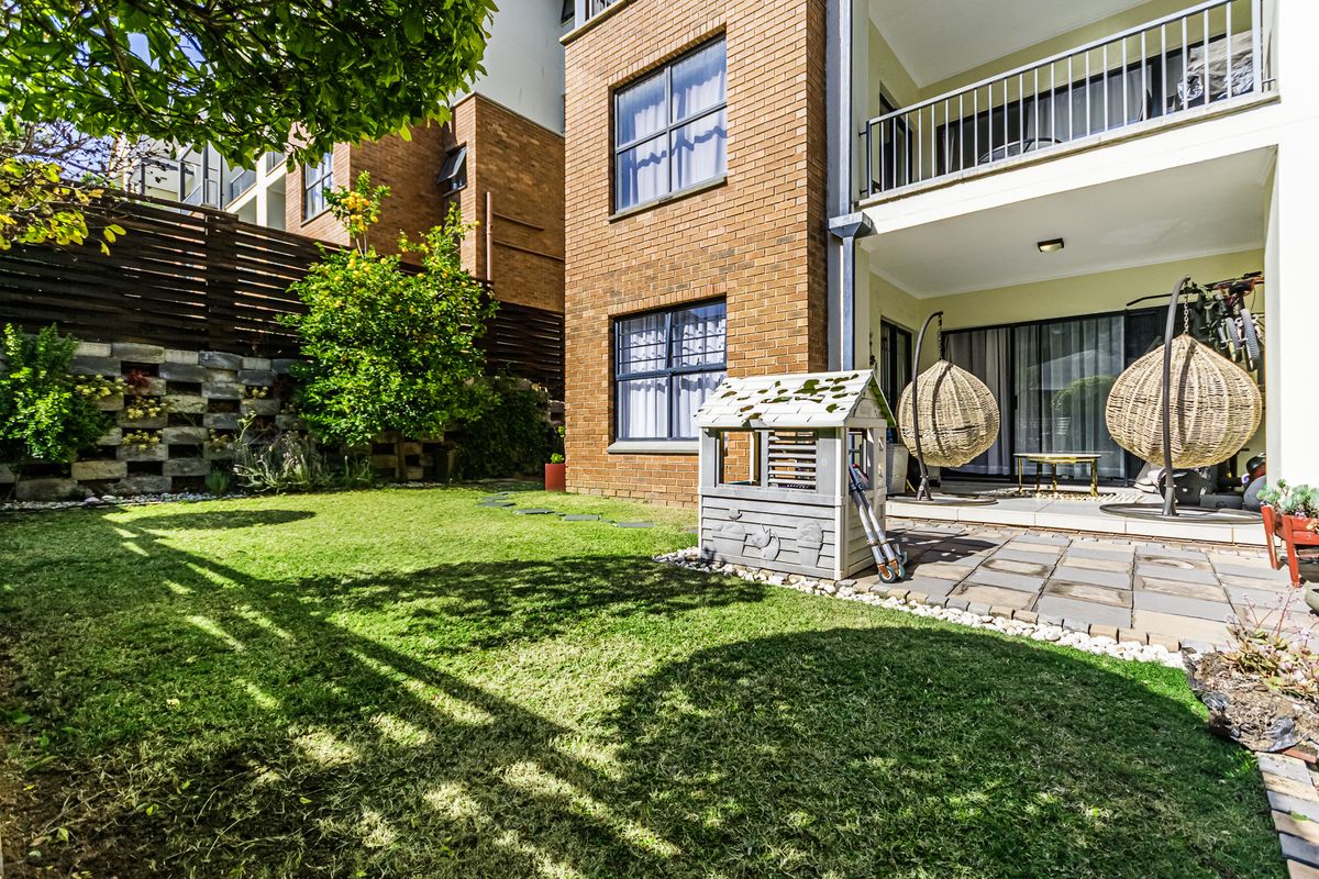 A private rear garden featuring a paved patio area, brick facade, and an elevated balcony, providing a functional outdoor space for the apartment.