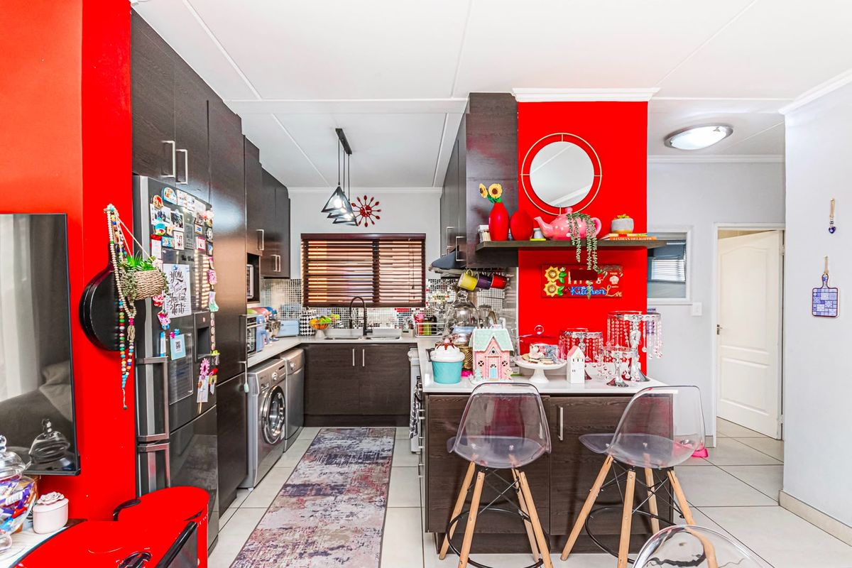 A functional kitchen featuring dark wood cabinetry, a mosaic tile backsplash, a central island, and integrated appliances, finished with bright red accent walls.