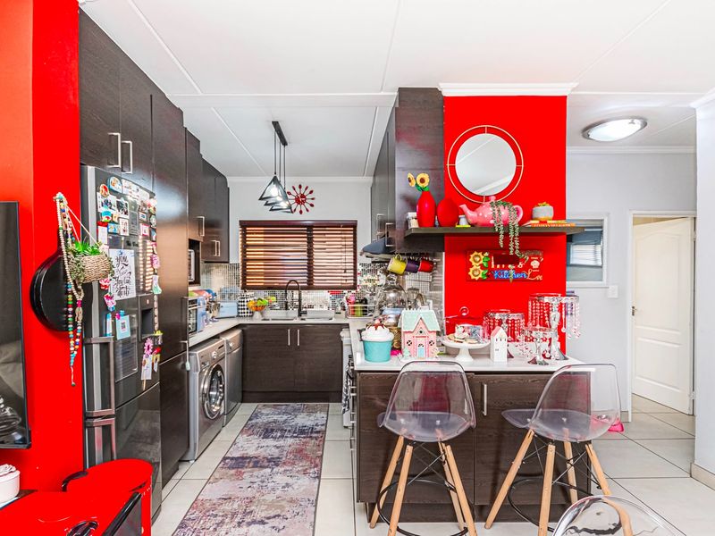 A functional kitchen featuring dark wood cabinetry, a mosaic tile backsplash, a central island, and integrated appliances, finished with bright red accent walls.