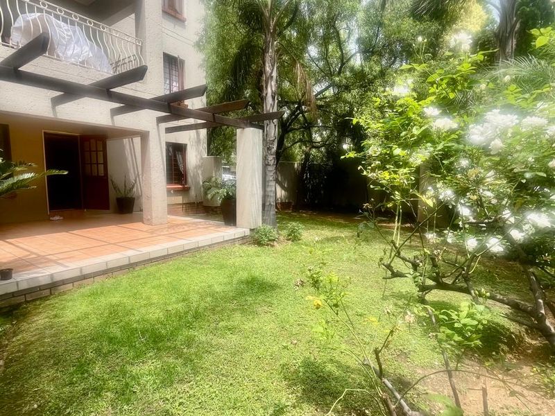 A private rear garden featuring a tiled patio with a timber pergola, overlooking a lush green lawn and established trees.