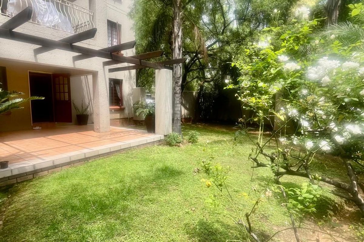 A private rear garden featuring a tiled patio with a timber pergola, overlooking a lush green lawn and established trees.