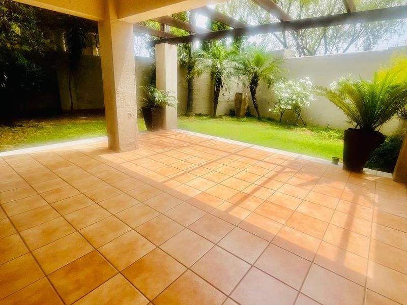 A covered patio area featuring tiled flooring and a timber pergola, overlooking a private garden space.