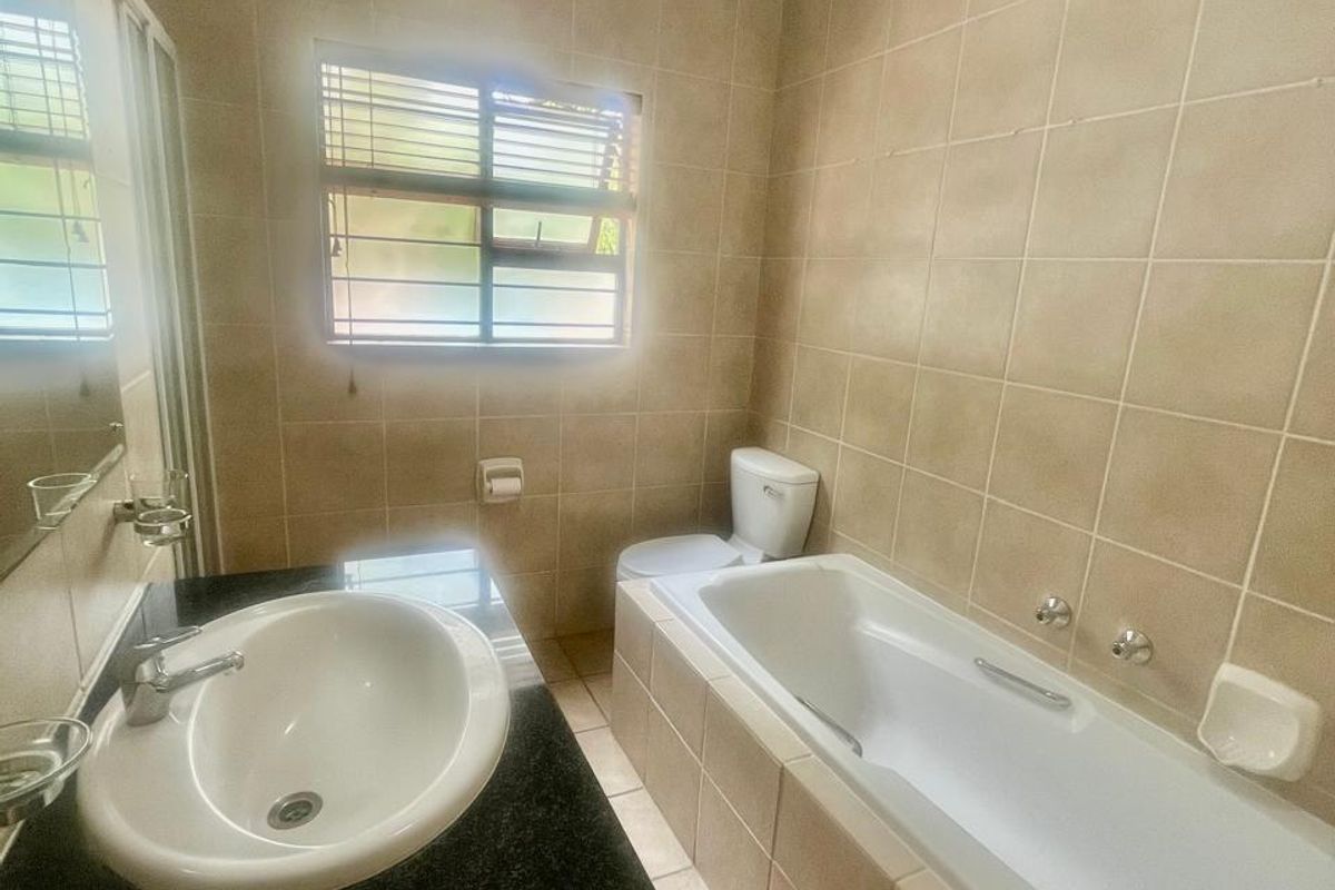 A functional bathroom featuring a built-in vanity with granite countertop, a drop-in basin, a bathtub, and neutral wall and floor tiling.