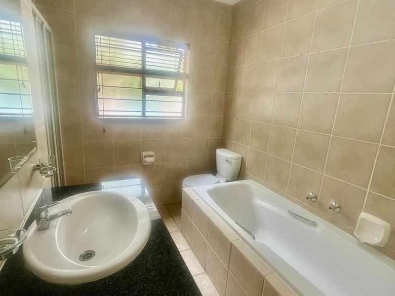 A functional bathroom featuring a built-in vanity with granite countertop, a drop-in basin, a bathtub, and neutral wall and floor tiling.