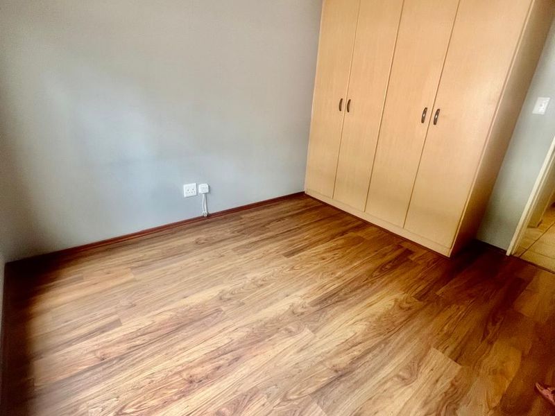 A bright, empty bedroom featuring warm-toned laminate flooring and a large, built-in wooden wardrobe with ample storage space.