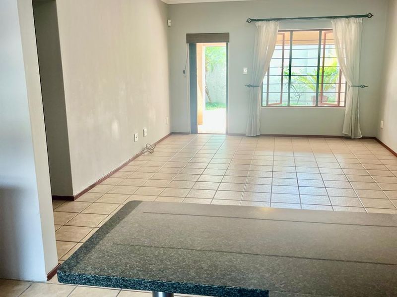 Spacious open-plan living area featuring tiled flooring, a granite breakfast counter, and direct access to an outdoor space.