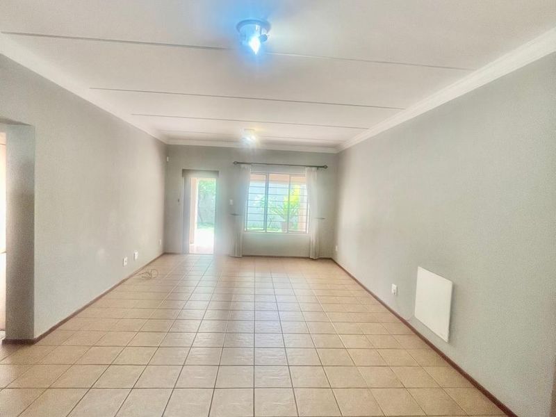 A spacious, empty living area featuring neutral wall tones, tiled flooring, and a wall-mounted heater, providing a clean canvas for interior design.