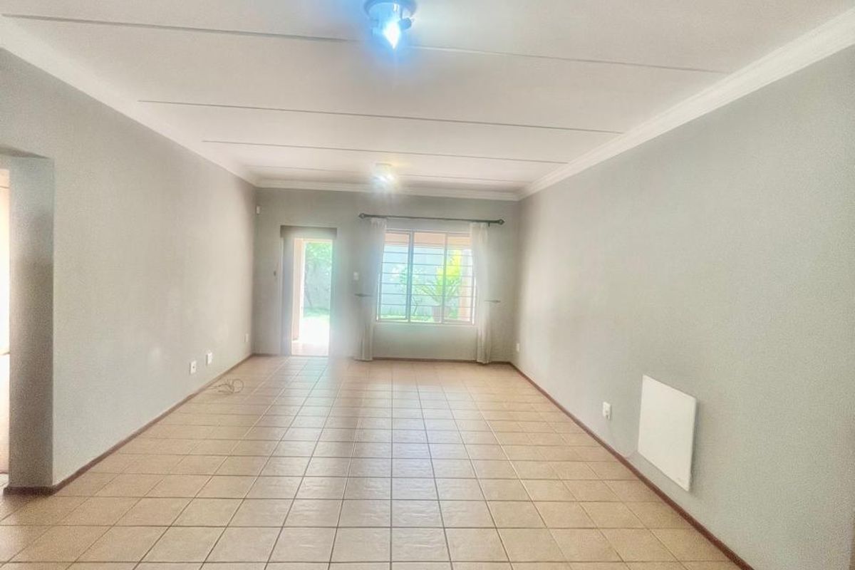 A spacious, empty living area featuring neutral wall tones, tiled flooring, and a wall-mounted heater, providing a clean canvas for interior design.