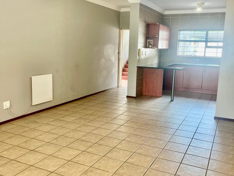 Open-plan living area featuring tiled flooring, a wall-mounted heater, and an adjoining kitchen with built-in cabinetry and a breakfast bar.