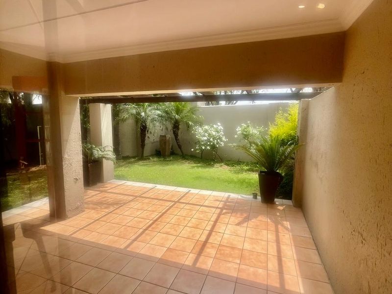 A covered patio area with tiled flooring, featuring a seamless transition to a private garden space.