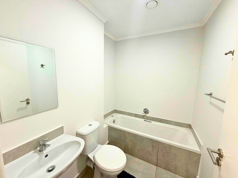 A clean and well-maintained bathroom featuring a built-in bathtub, pedestal washbasin, and neutral ceramic tiling throughout.