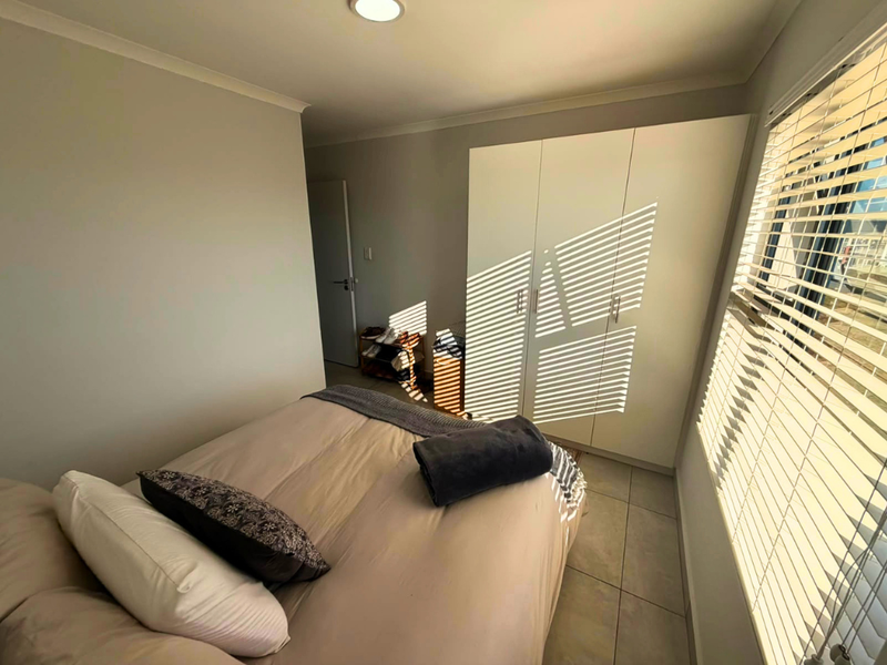 A bright bedroom featuring tiled flooring, built-in wardrobes, and venetian blinds that allow natural light to filter into the space.