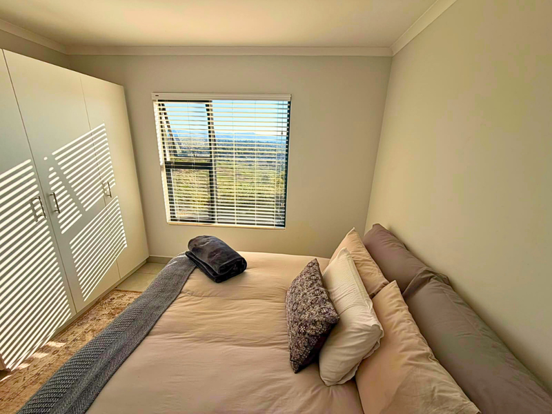 A well-lit bedroom featuring built-in wardrobes, tiled flooring, and a window with venetian blinds offering scenic views.