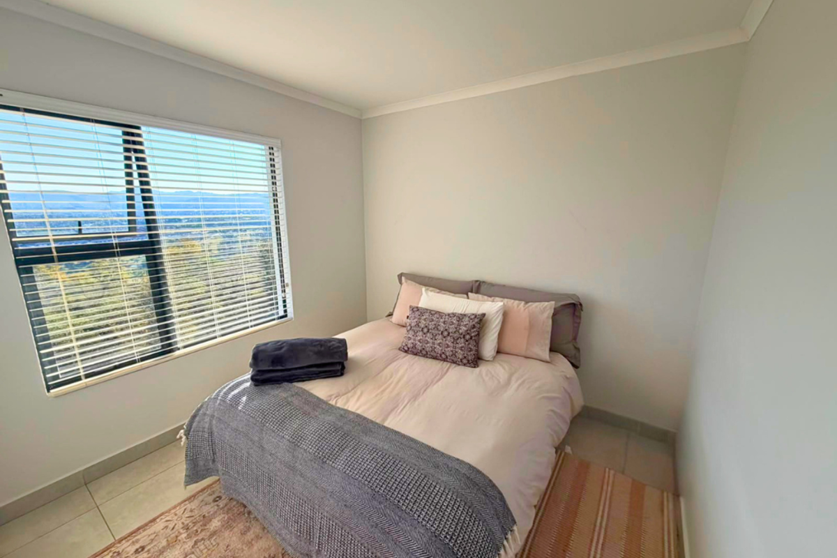 A bright bedroom featuring tiled flooring, coved ceilings, and an aluminium window with venetian blinds offering scenic views.