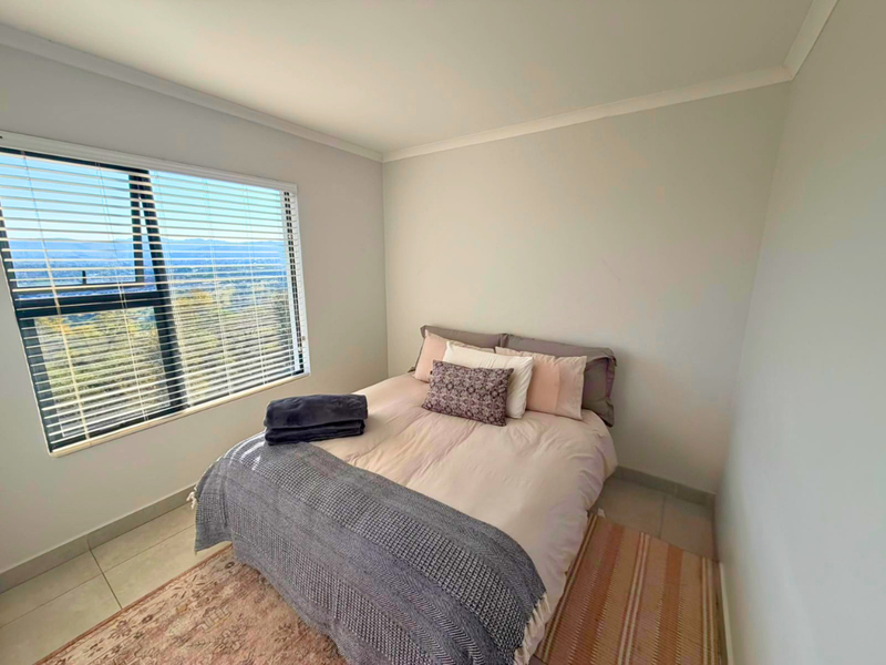 A bright bedroom featuring tiled flooring, coved ceilings, and an aluminium window with venetian blinds offering scenic views.