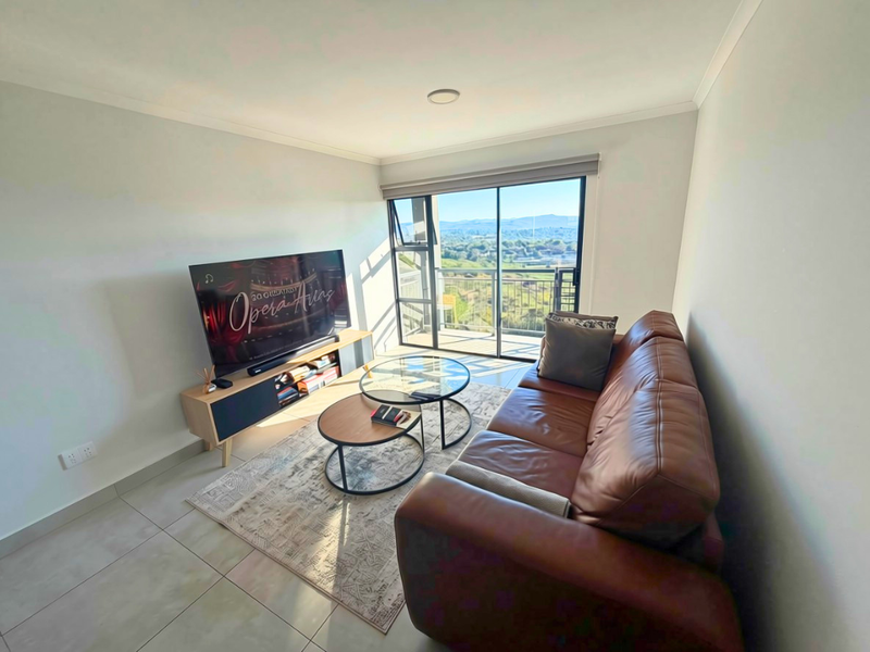 A bright living room featuring tiled flooring and a large sliding glass door that opens to a balcony with scenic views.