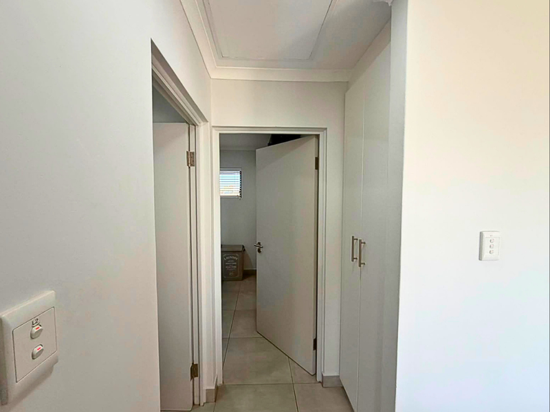 A clean, neutral hallway featuring tiled flooring and built-in storage cabinetry, providing access to adjacent rooms.