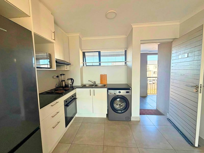 Modern kitchen featuring built-in cabinetry, electric hob, oven, extractor fan, and double sink, with tiled flooring and direct access to the apartment entrance.