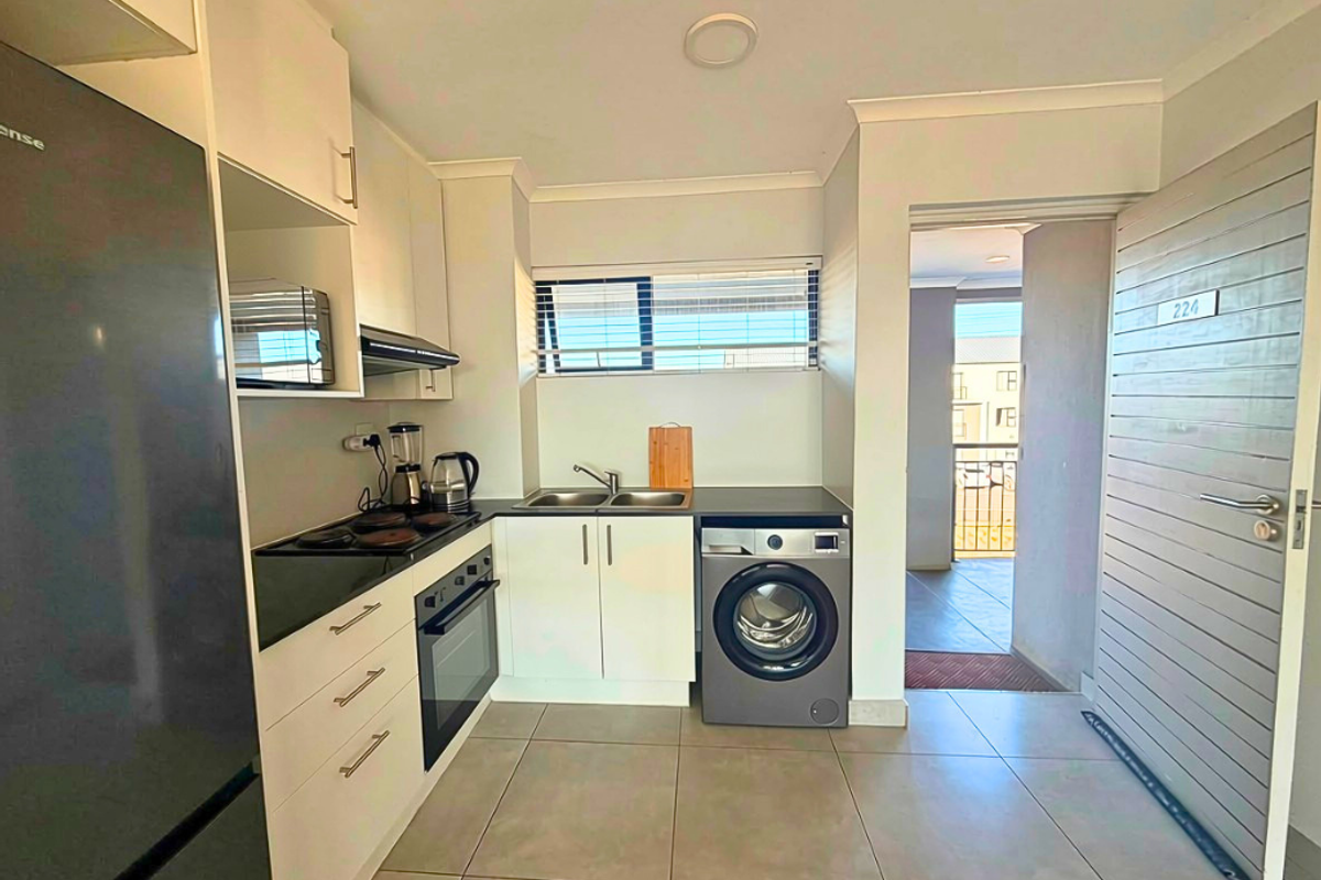 Modern kitchen featuring built-in cabinetry, electric hob, oven, extractor fan, and double sink, with tiled flooring and direct access to the apartment entrance.