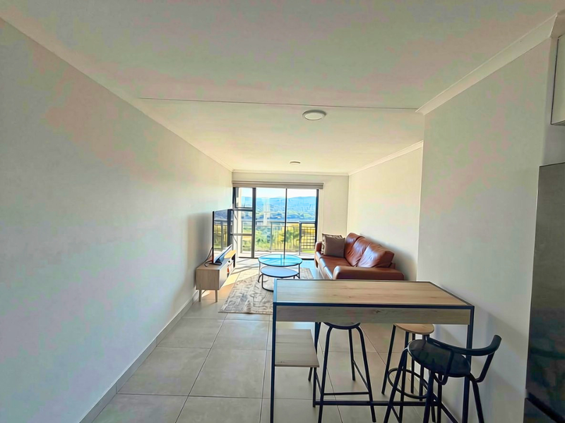 Open-plan living area featuring tiled flooring, recessed lighting, and a sliding glass door leading to a balcony with scenic views.