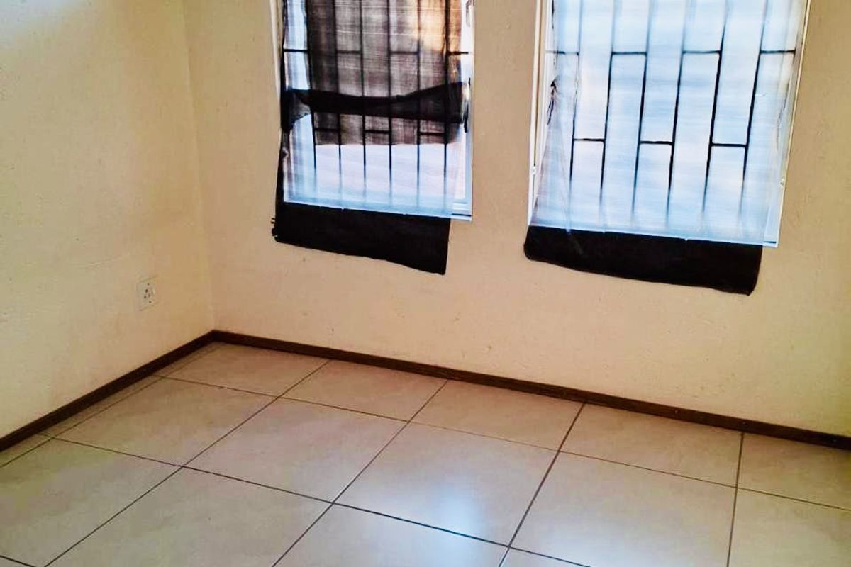 An empty bedroom featuring tiled flooring and windows fitted with security bars, offering a blank canvas for potential renovation or staging.