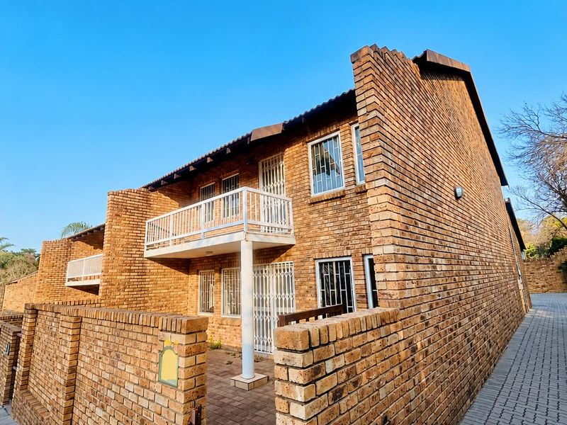 A well-maintained face brick townhouse exterior featuring a paved entrance, security gates, and an upper-level balcony.