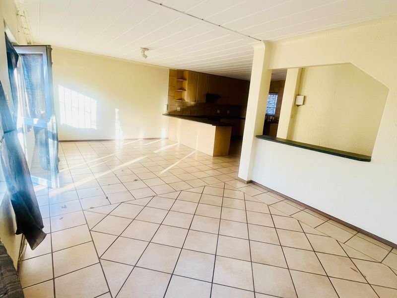 An open-plan living and kitchen area featuring tiled flooring, a breakfast bar, and dated cabinetry, offering a blank canvas for renovation.