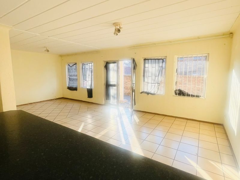 Spacious open-plan living area featuring tiled flooring, security bars on windows, and direct access to the exterior.