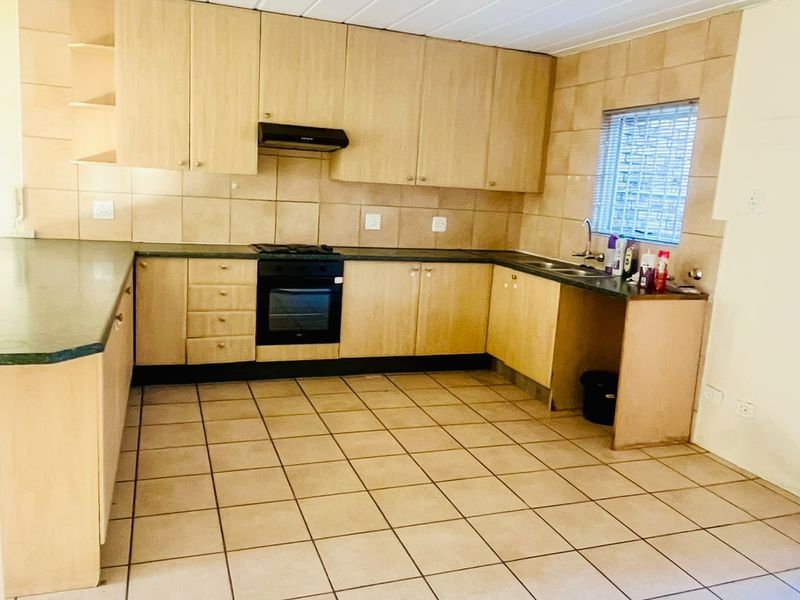 A functional kitchen featuring light wood cabinetry, laminate countertops, built-in oven with hob, and tiled flooring throughout.