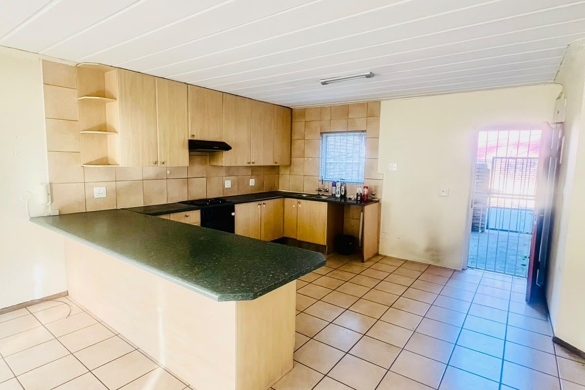 A functional kitchen featuring laminate cabinetry, tiled flooring, and a breakfast bar, with direct access to an exterior area through a security gate.