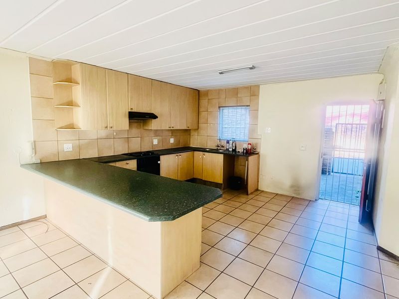 A functional kitchen featuring laminate cabinetry, tiled flooring, and a breakfast bar, with direct access to an exterior area through a security gate.