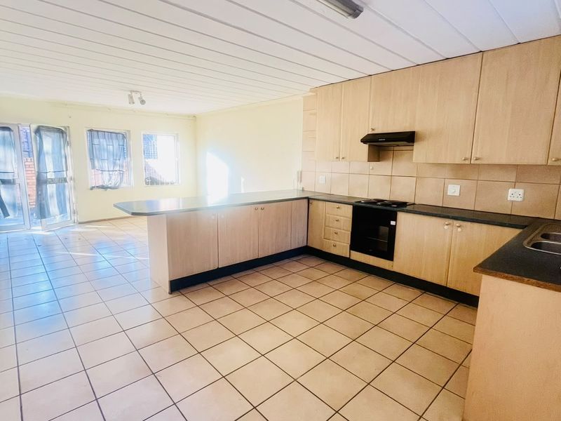 Spacious open-plan kitchen and living area featuring light wood cabinetry, dark countertops, tiled flooring, and a functional layout with integrated cooking appliances.